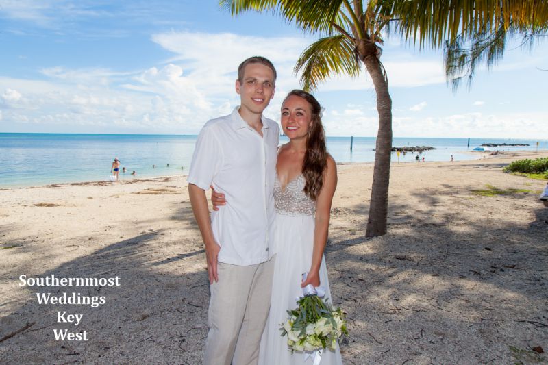 Wedding couple stand under a palm tree next to the ocean at Ft. Zachary Taylor State Park in Key West, Florida