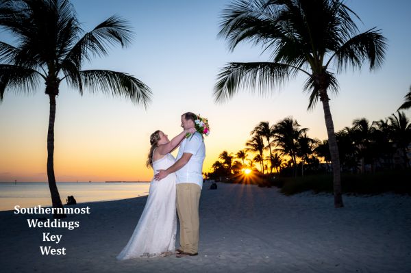 Wedding couples poses between to palm trees at sunset on Smathers Beach in Key West, FL.